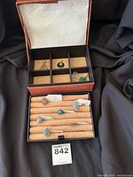 Open jewelry box with internal ring tray and compartments visible, rings in tray and pendants in upper grid