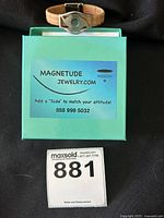 Full lot with Magnitude cork bracelet resting on branded box with seller's lot number card.