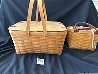 Photo showing the Reunion Picnic Basket with wood handles and the Medium Boardwalk Basket with leather handles on a black cloth background.