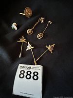 Six assorted Masonic pins placed on black cloth background, showing various designs and styles.