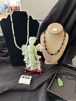 Photo of two necklaces on busts and jade-like carved statue with wood base in front