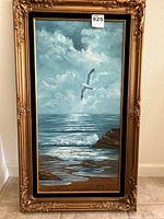 Full view of the vertical oil painting showing a seagull flying over waves, rocky shore, and cloudy sky in a detailed ornate gold frame.