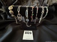 Set of six costume bracelets and one necklace displayed on a black velvet stand, showing variety of styles and materials.