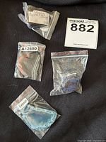 Four items in small plastic bags with labels, including stone pendants and crystals, alongside lot number card
