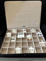 Open black faux suede jewelry box with beige interior showing 10 pairs of gemstone earrings in various compartments.