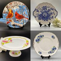Four-piece set including two floral patterned cake plates, cake server, and a pedestal plate stand photographed against a black backdrop.