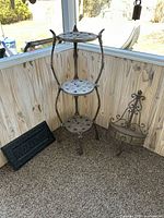 Cast iron 3-tier plant stand next to metal Welcome sign and bronze wall shelf in corner of screened porch
