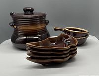 Full view of one brown ceramic tureen with lid, four appetizer dishes stacked, and two French onion soup bowls side by side.