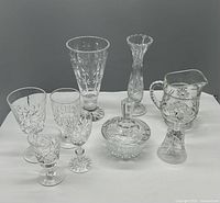Full lot of crystal items including vases, candy dish, bell, pitcher and wine glasses on white tablecloth