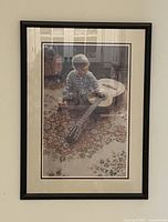 Framed watercolour print showing a child with a guitar sitting on a patterned rug indoors, with a black frame and double matting.