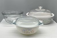 Front view of three bowls including Pyrex Blue Irises casserole bowl with lid, Classic Elegance Corning casserole dish with lid, and one clear Anchor Hocking bowl.