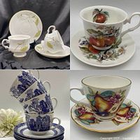 Varied tea cups and saucers arranged on black cloth showing different patterns of fruit and floral decoration