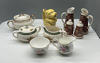 Photo of assorted vintage sugar, creamer, condiment items including dog-shaped mustard pot and ceramic salt and pepper shakers