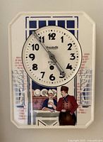 Full view of the porcelain wall clock showing the entire clock face and Dutch scene painting below it, mounted on a white wall.