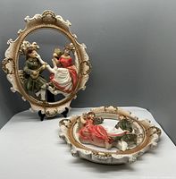 Both chalkware wall hangings displayed on a surface, showing the front details and frame design