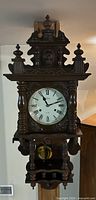 Full front view of carved wooden wall clock showing columns, finials, pendulum and shelf