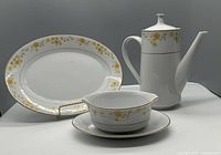 Platter, gravy boat with attached underplate, and coffee pot shown with white background highlighting yellow floral pattern and gold rim.