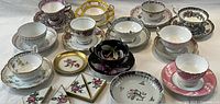Photo of all tea cups, saucers, blotter corners, and trinket dishes arranged on white surface showing variety of styles and colors including floral and gold accents.