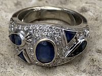 Front view showing central oval sapphire, surrounding pavé diamonds, and side sapphire accents