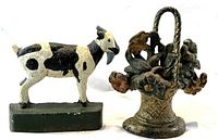 Two cast iron decorative doorstops together: flower basket doorstop with visible floral detail and curved handle and Billy goat doorstop painted in black and white standing on a green base.