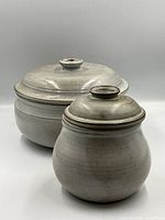 Both handmade lidded pottery jars shown from the front, large in back and smaller in front.