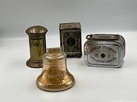 Four vintage and antique coin banks displayed showing overall size and details including a bell-shaped bank and cylindrical brass bank.