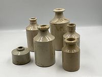 Front view of six off-white glazed stoneware bottles and inkwell forms on white background