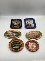 All six small vintage beer advertising serving trays arranged in two rows on white background