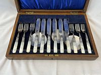 Set of 6 forks and 6 cutting utensils displayed inside original wooden box lined with blue velvet.