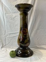 Full view of the antique ceramic pottery stand showing floral hand decorations and dark green finish, with green apple for scale.