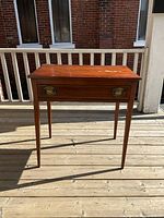 Front view of antique wooden side table showing single drawer with original brass oval pulls, tapered legs, and surface wear on top.