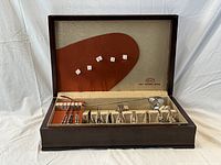 Wooden hinged flatware box open showing compartments with knives, forks, spoons and serving pieces