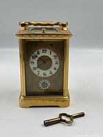 Front view of brass carriage clock and winding key on white background