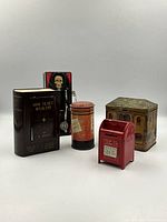 Group photo showing five antique and vintage metal coin banks including the skeleton windup bank, book-shaped bank, cylindrical bank, red mailbox bank, and building-shaped bank.