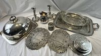 Overview of the collection showing the meat dome with tray, candlestick holders, pitcher, condiment container, decorative serving trays and various trivets.