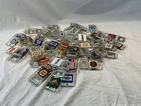 Overview photo showing the complete collection of 49 vintage beer bottle openers spread out on a white cloth background. Each has a clear plastic casing with a metal opener and a variety of advertising labels.