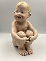 Front view of the large 10 inch bisque statue showing the smiling child seated with arms wrapped around knees and facial details.
