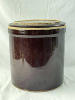 Photo of large antique stoneware crock standing upright showing dark brown glaze and tan rim.