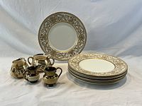 Seven Royal Worcester bone china dinner plates stacked with ornate gold Florentine design and four pairs of antique Gibson Staffordshire lustre ware creamers arranged in front of plates against white backdrop.