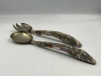 Two salad serving utensils with mother of pearl inlaid curved handles resting on a white background.