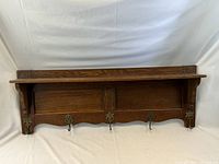 Full view of the oak coat rack showing the shelf and four hooks underneath mounted on a white backdrop.