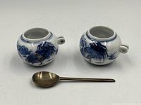 Pair of blue and white porcelain bird feeder holders shown with spoon on white surface to display size and detail