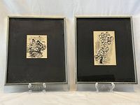 Pair of framed ink sketches side by side on clear display stands