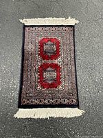 Full view of handmade red prayer rug with cream and black borders and fringes at both ends.