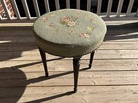 Full front view of round wooden stool with handcrafted floral needlepoint cushioned seat.