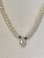 Close-up detail of the teardrop pearl pendant with adjacent dark beads on the pearl strand.