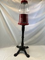 Front view of vintage red gum machine with clear glass globe atop a decorative black stand.