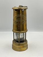 Full view front of brass cylindrical coal mining lamp on white background