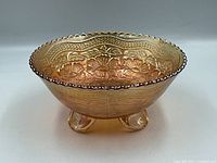 Side view of the marigold-colored carnival glass footed candy dish with scalloped edge and detailed pressed floral pattern.