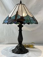 Full view of vintage Tiffany style lamp with stained glass dragonfly motif and ornate heavy base, plugged in and lit.